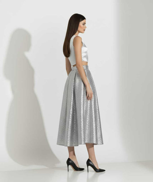 Woman wearing a white sleeveless top and silver metallic skirt on a white background