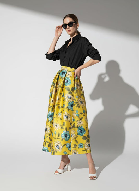 Woman wearing a black blouse and yellow floral skirt against a white background