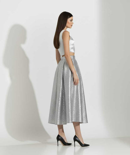 Woman wearing a white sleeveless top and silver metallic skirt on a white background