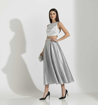 Woman wearing a silver top and skirt with a clutch against a white background