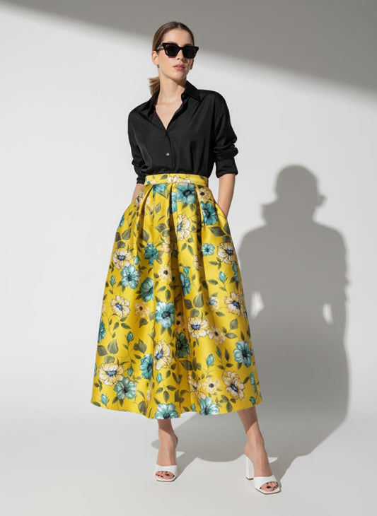 Woman wearing a black shirt and yellow floral skirt against a white background